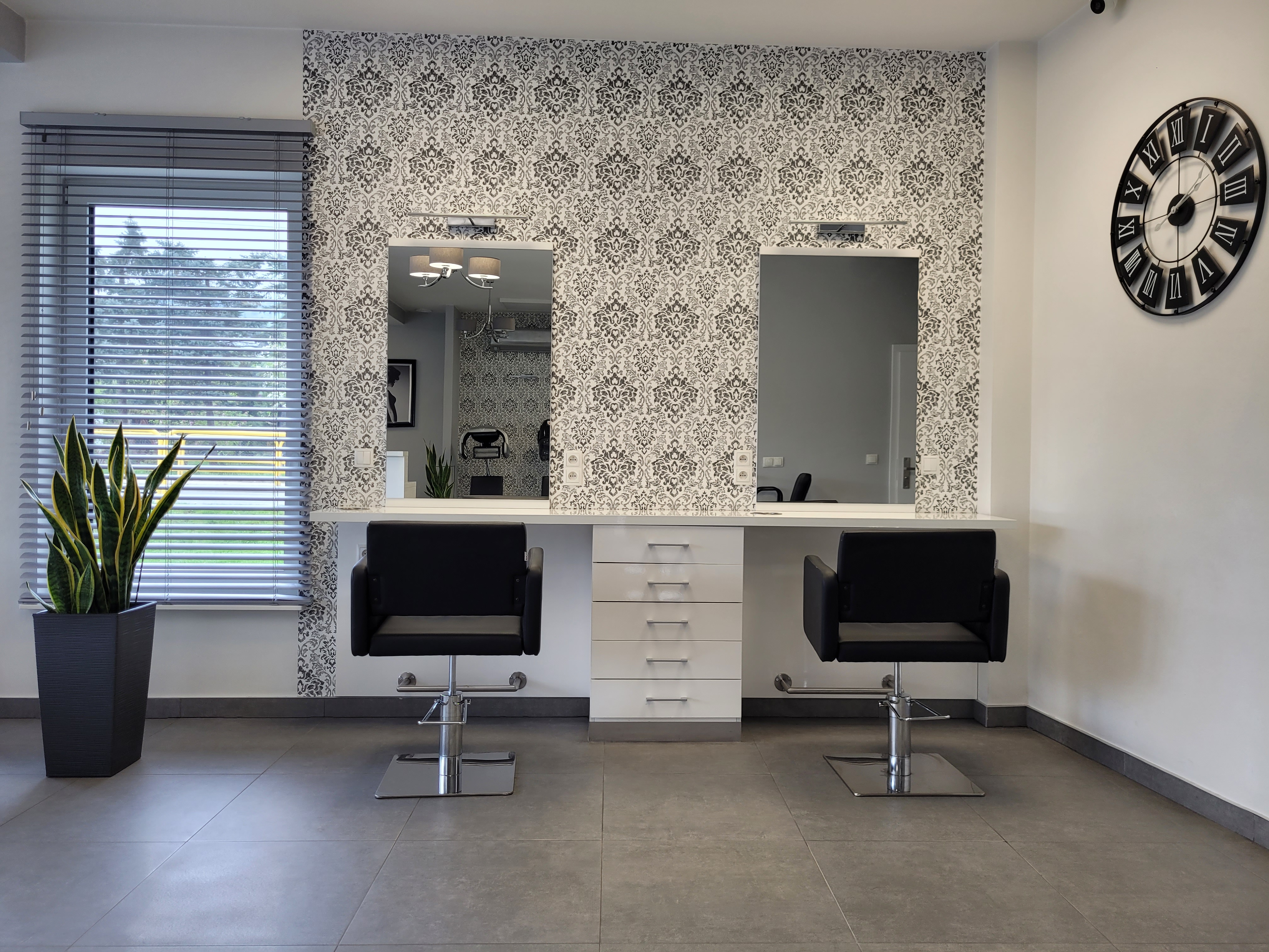 Czarno-białe wnętrze salonu fryzjerskiego z czarnymi fotelami i stanowiskami pracy przy lustrach, wyróżnionymi tapetą w stylu retro.