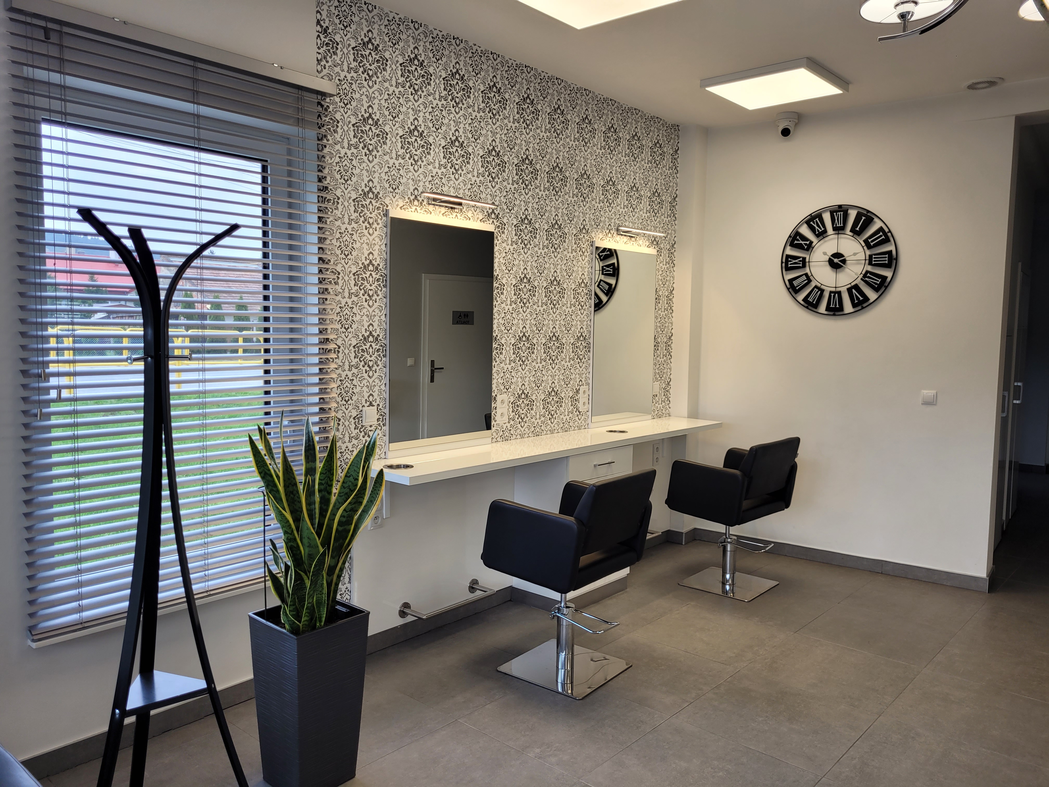 Czarno-białe wnętrze salonu fryzjerskiego z czarnymi fotelami i stanowiskami pracy przy lustrach, wyróżnionymi tapetą w stylu retro.